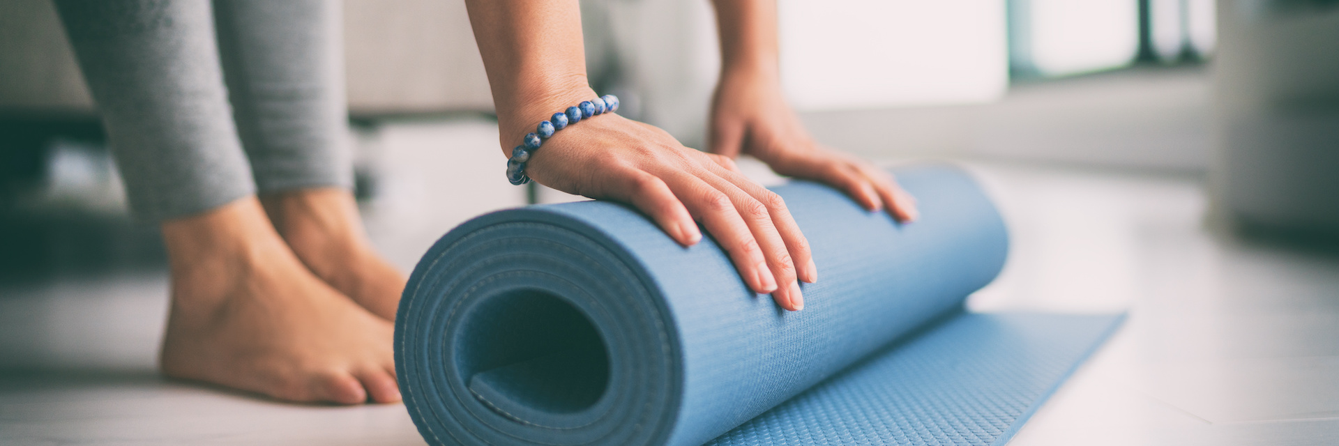 Pilates-Matte wird ausgerollt Eine Frau rollt eine blaue Pilates-Matte auf dem Boden aus.